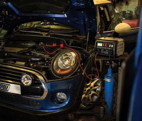 Blue car with open hood in a garage setting, showing electrical work.