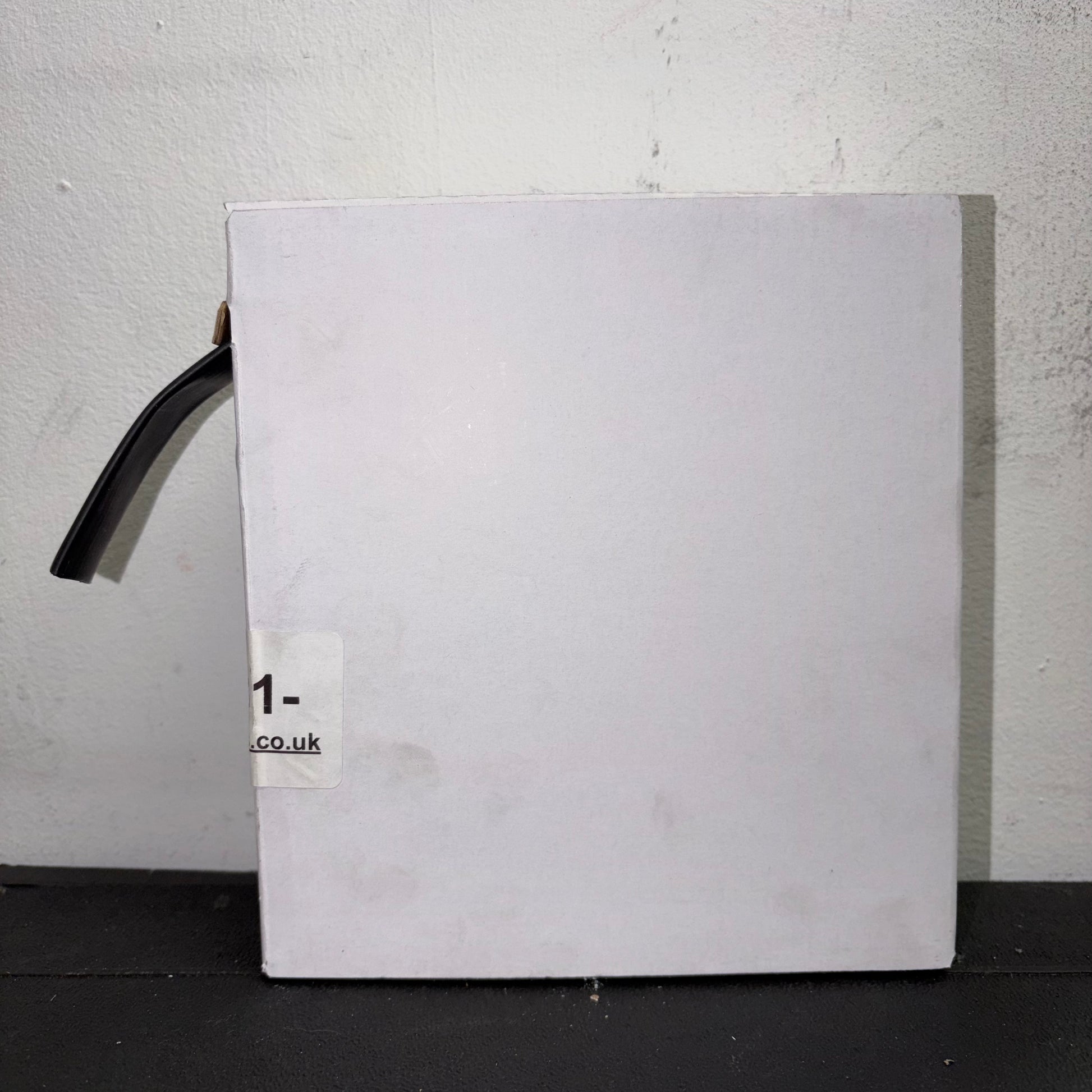 Front view of a white mini reel box containing black adhesive-lined heatshrink tubing sticking out from the side slot.