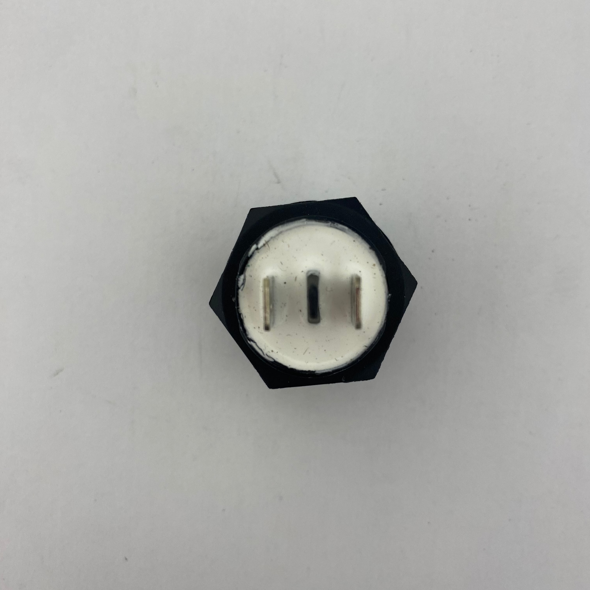 Black push botton momentary switch with a white center on a light gray background