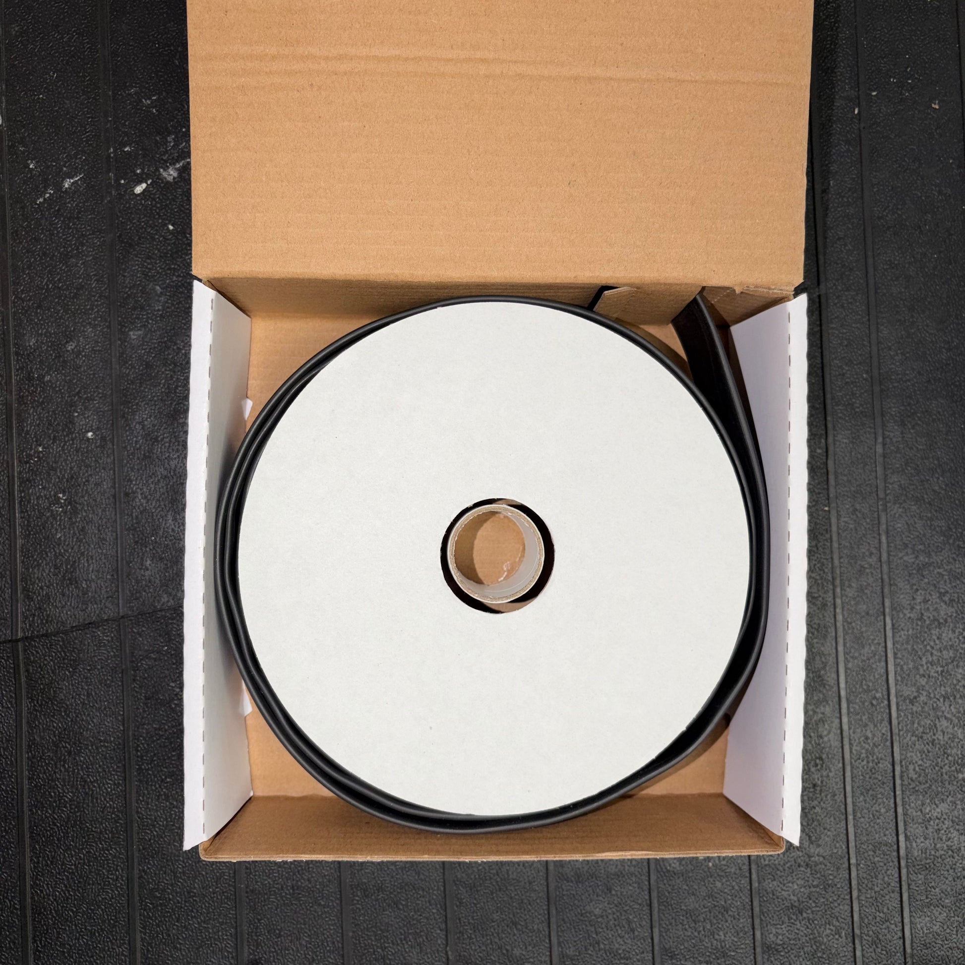 Top-down view of a spool of black heatshrink tubing inside an open cardboard box.