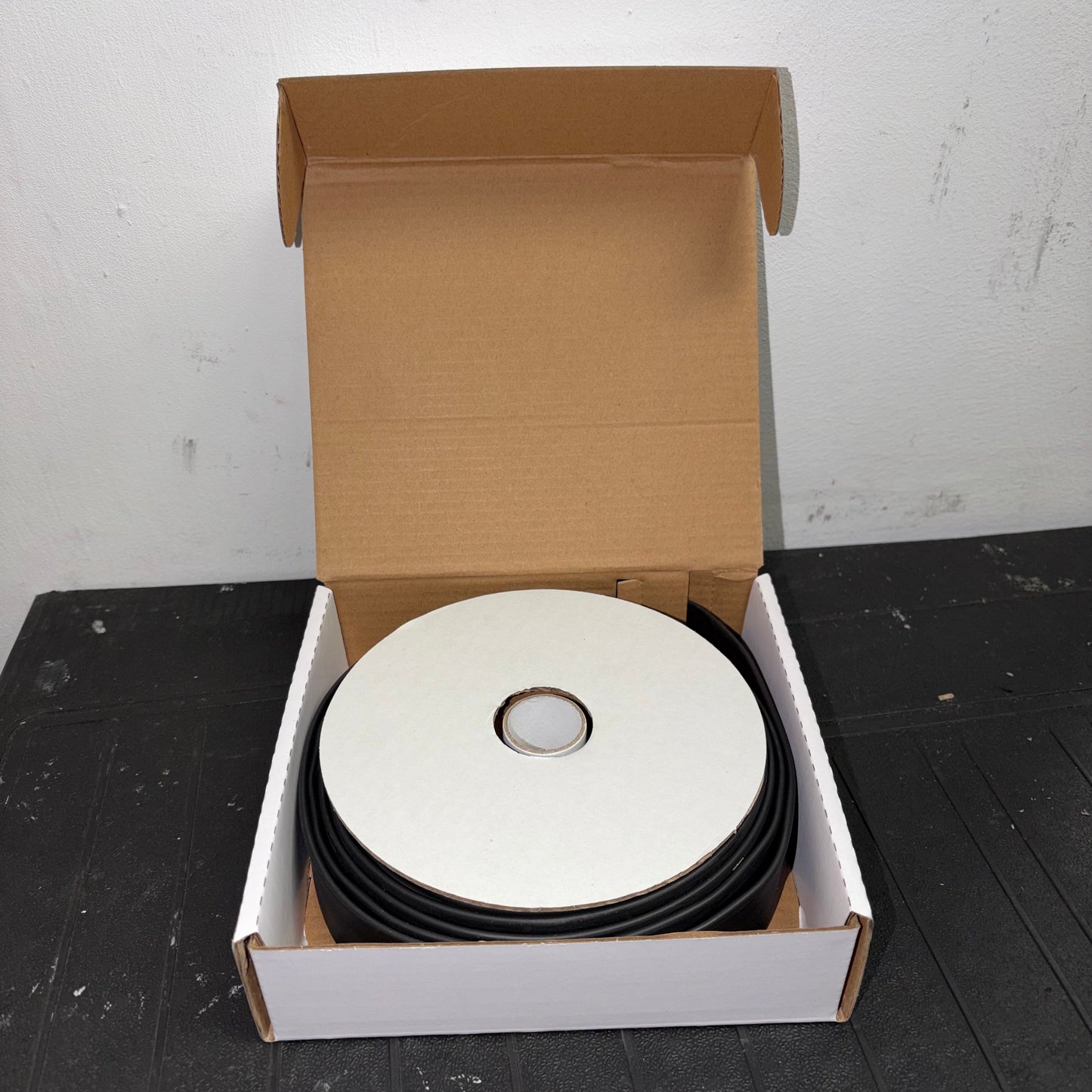 Open box containing a mini reel of black heatshrink tubing with white cardboard packaging.
